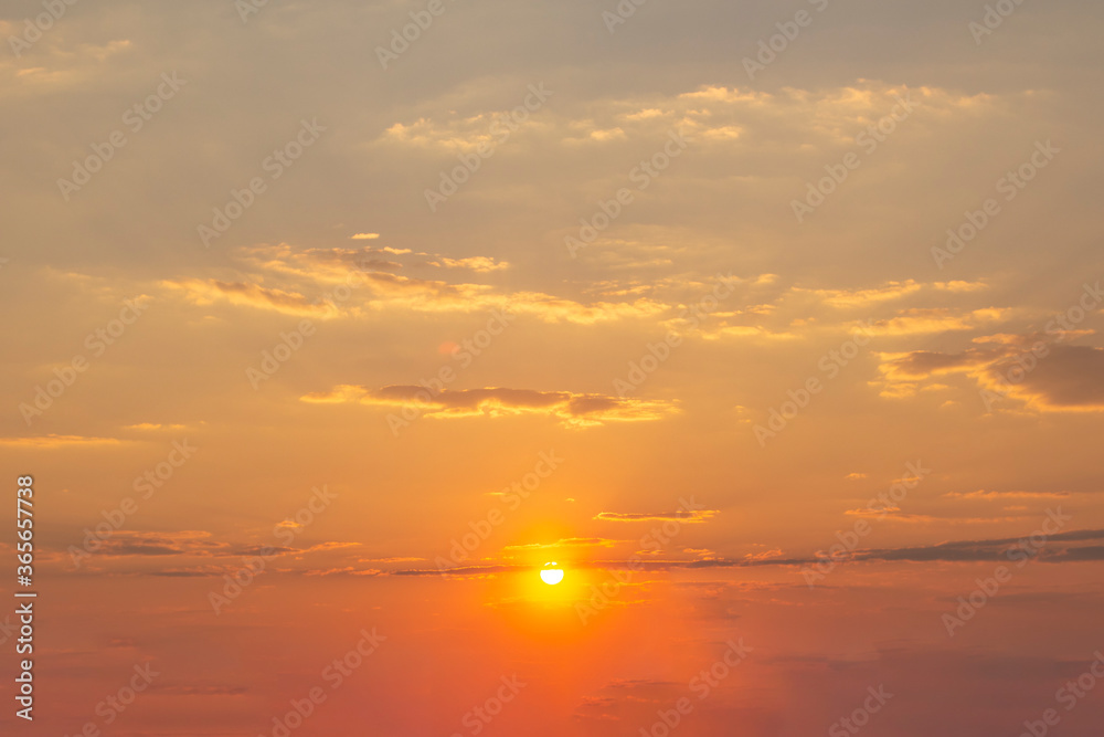 Orange sunset sky with sun and light clouds.