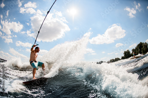 athletic man wakesurfing on the river and pulled by a boat. © fesenko