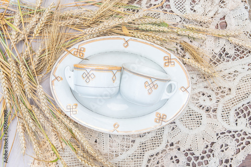 Antique fayence plate and pair of mugs with the same yellow pattern - countryside porcelain objects with wheat cereal on lace tableclothes photo