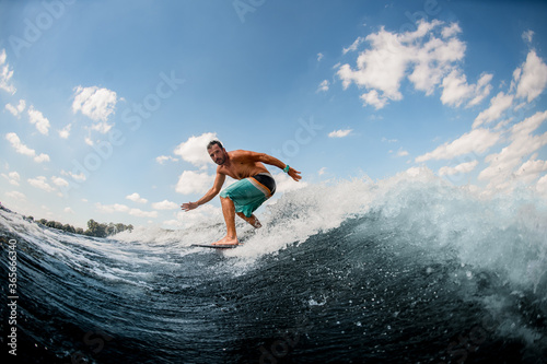 athletic guy wakesurfer actively ride on the waves on surfboard against blue sky