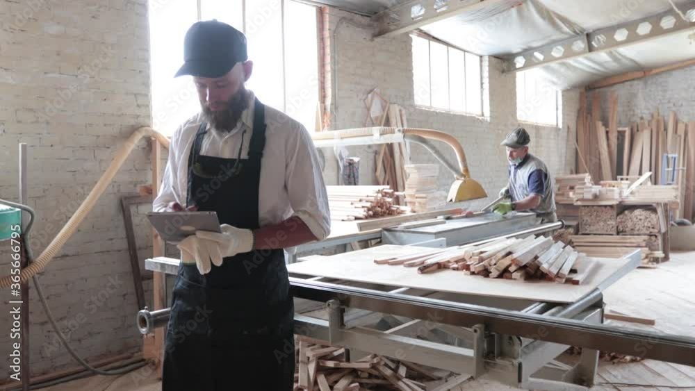 Carpenter in his own woodshop using a tablet pc and writes notes while being in his workspace. Small business concept Carpenter in his own woodshop using a tablet pc and writes notes while being in his workspace. Small business concept