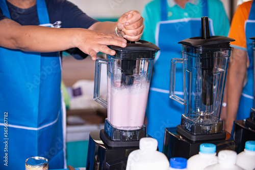 The vendor is making fruit smoothies for sale.