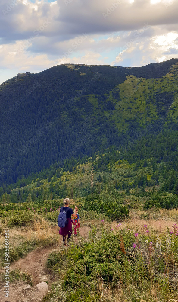 A woman and a child are going down the mountainside along the path. Mountain in the background A woman and a child are going down the mountainside along the path. Mountain in the background