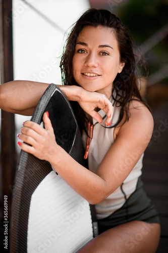 portrait of pretty girl which leans her hands on surfboard and looks at camera