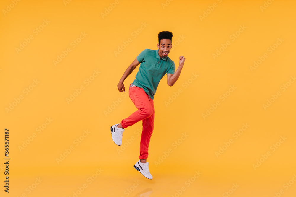 Full-length shot of inspired black guy dancing in red pants. Indoor photo of carefree african man enjoying photoshoot on yellow background.