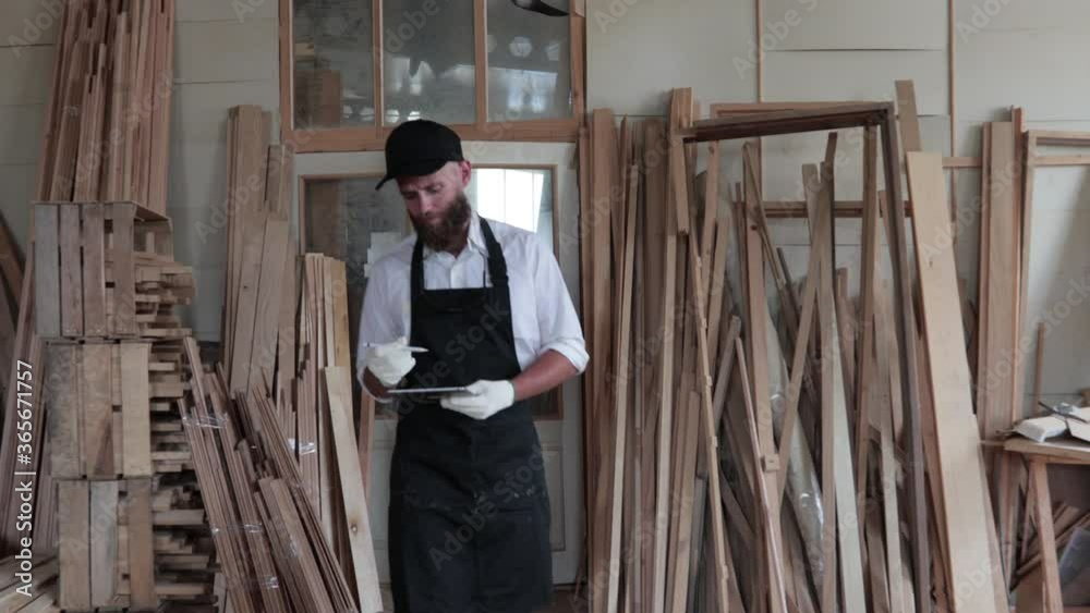 Carpenter in his own woodshop using a tablet pc and writes notes while being in his workspace. Small business concept Carpenter in his own woodshop using a tablet pc and writes notes while being in his workspace. Small business concept