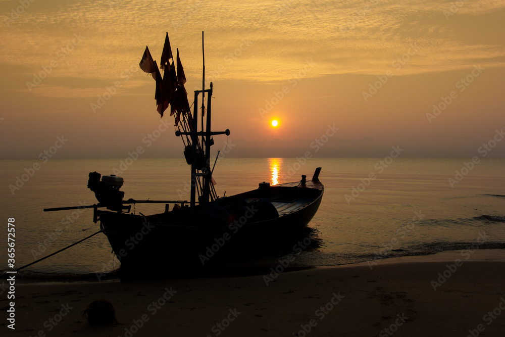 Silhouette of a fishing boat bound on a beach with sunrise in the morning, fresh orange sky.