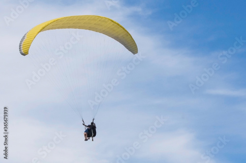 Two paragliders are flying in tandem against a blue sky. Copy space.