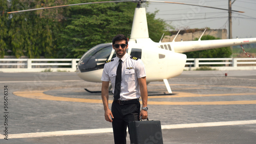 Pilot in uniform standing near small private helicopter
