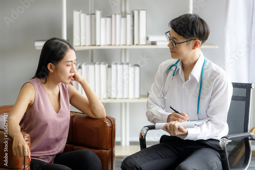 Young Asian male doctor is recording a medical history on the clipboard and explaining something to the female patient. Medical and health care concepts