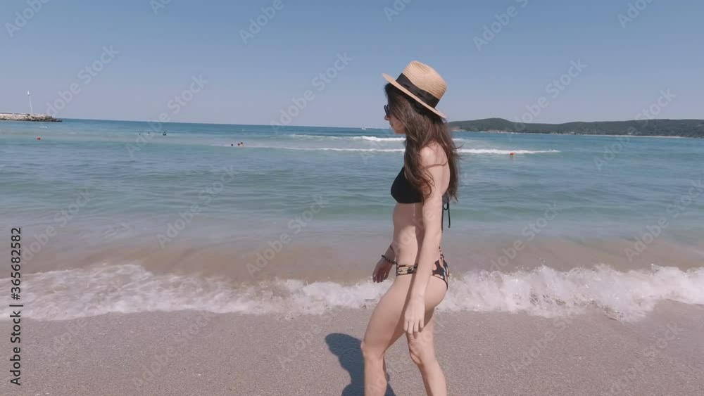 Fit Athletic woman with sun hat and bikini swimsuit walking barefeet on sand the beach and entering the sea Fit Athletic woman with sun hat and bikini swimsuit walking barefeet on sand the beach and entering the sea
