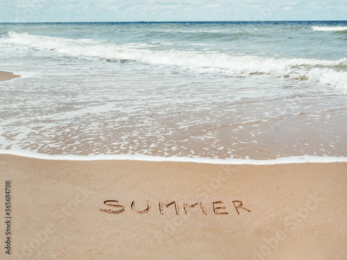 Sea coast with soft surf. Word SUMMER written on sandy beach. Summer vacation on seaside.