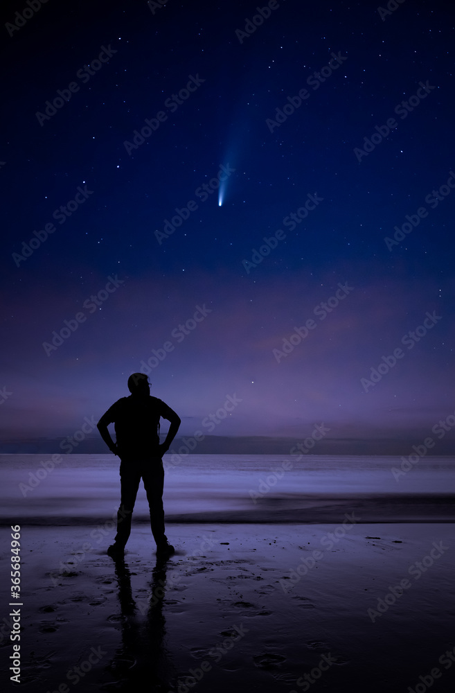 Watching comet NEOWISE high in the sky by a man on a beach during night