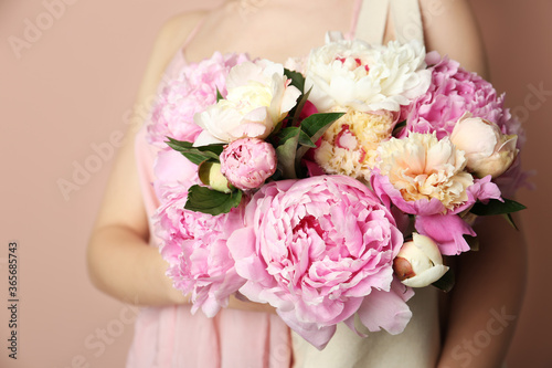 Woman with bouquet of beautiful peonies in bag on beige background, closeup