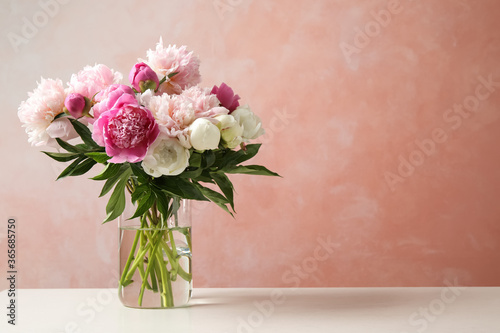 Beautiful peony bouquet in vase on table against pink background. Space for text