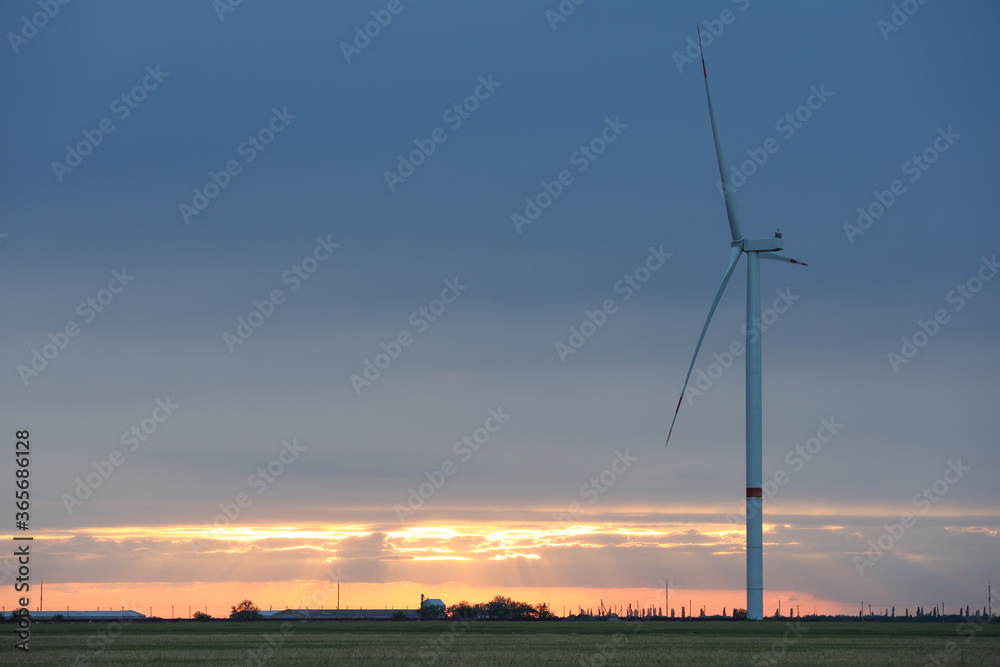 Obraz premium Beautiful view of field with wind turbine at sunset. Alternative energy source