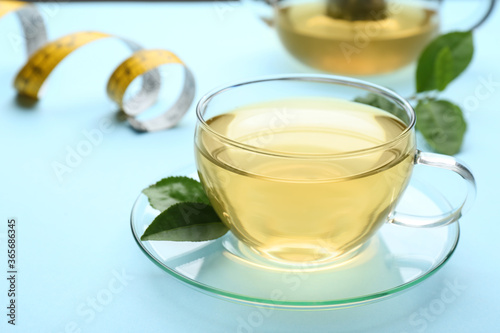 Glass cup of diet herbal tea and green leaves on light blue background