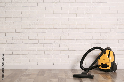 Modern yellow vacuum cleaner on wooden floor near white brick wall  space for text