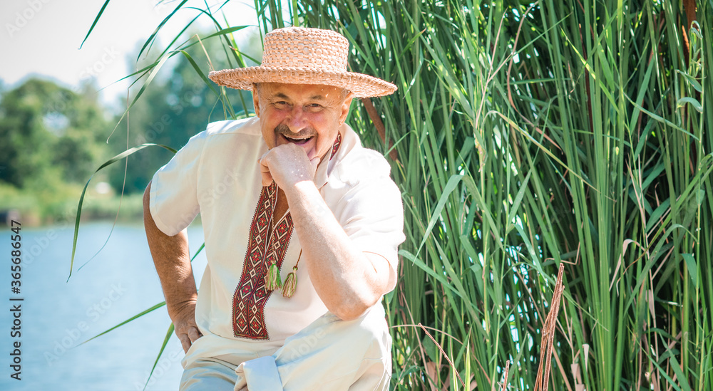 Φωτογραφία Happy senior man in embroidered skirt and straw hat at nature rest, lifestyle of