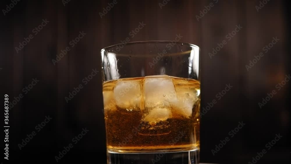 Close-up of a misted-up glass of whiskey with ice slowly spinning around on a wooden background. The concept of the celebration and alcohol. Close-up of a misted-up glass of whiskey with ice slowly spinning around on a wooden background. The concept of the celebration and alcohol.