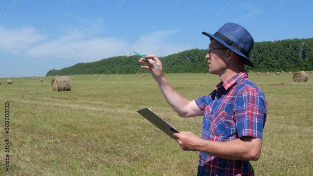 A male farmer counts bales of hay and writes the result in a notebook.