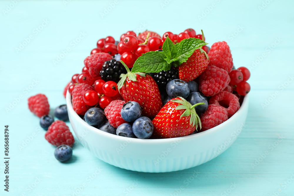 Mix of different fresh berries and mint in bowl on light blue wooden table Mix of different fresh berries and mint in bowl on light blue wooden table