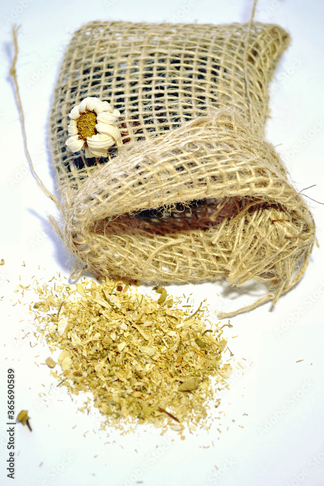 Dried chamomile flowers in balk next to the small jute sack isolated against white-grey background. Closeup.  Herbal traditional medicine. Relax tea. Healthy life style. Phytotherapy