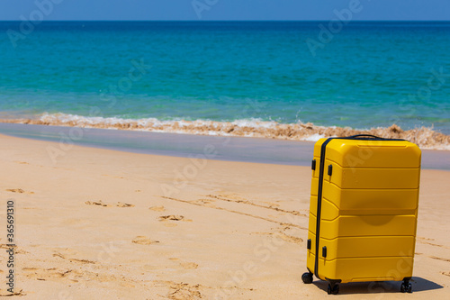 Yellow tourist suitcase on the beach near the blue water. © dadoodas