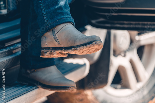 Girl sits in car with her legs dangling in jeans and hiking boots after hike.