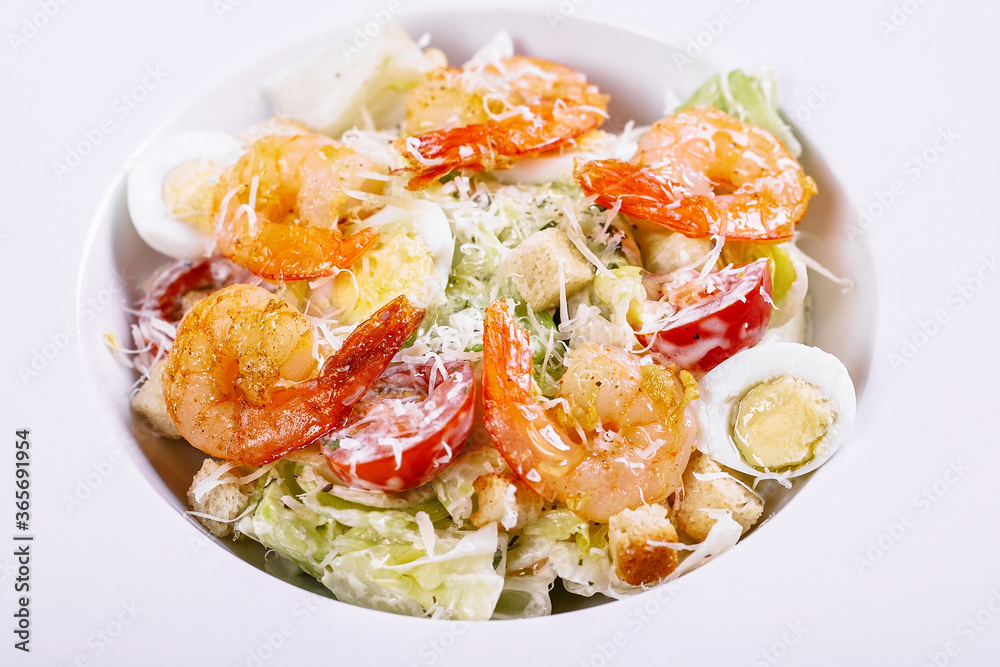 Caesar salad with fried shrimps and parmesan cheese on a white plate. Close-up. Caesar salad with fried shrimps and parmesan cheese on a white plate. Close-up.