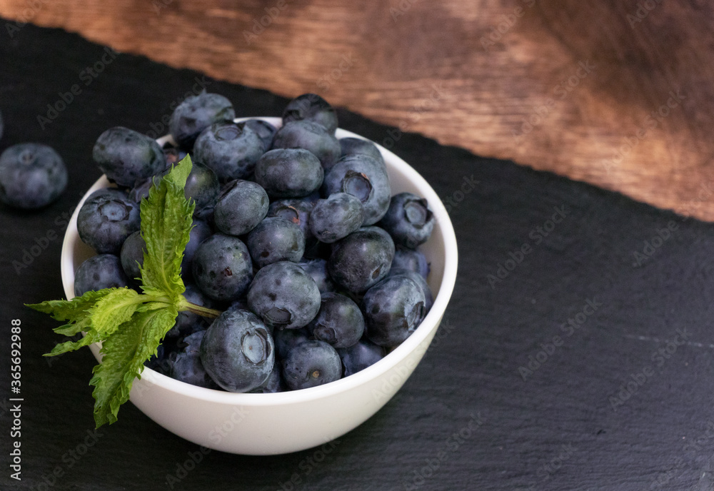 Blueberries with mint leaves in a small white bowl. On a black granite board. Yummy. Blueberries with mint leaves in a small white bowl. On a black granite board. Yummy.