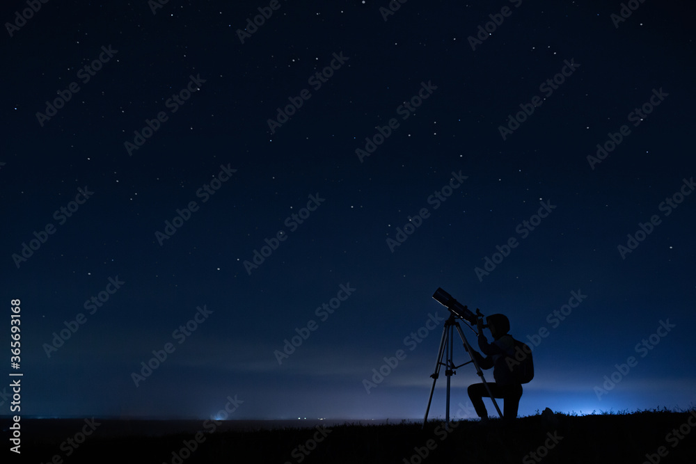 Human silhouette and telescope, a woman looks through a telescope at the starry sky. Night sky, stars, long exposure, astronomy