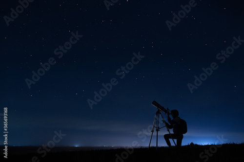 Human silhouette and telescope, a woman looks through a telescope at the starry sky. Night sky, stars, long exposure, astronomy photo