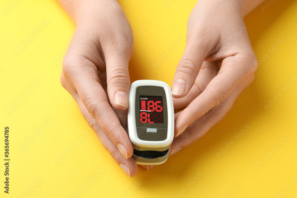 Woman holding fingertip pulse oximeter on yellow background, closeup Woman holding fingertip pulse oximeter on yellow background, closeup
