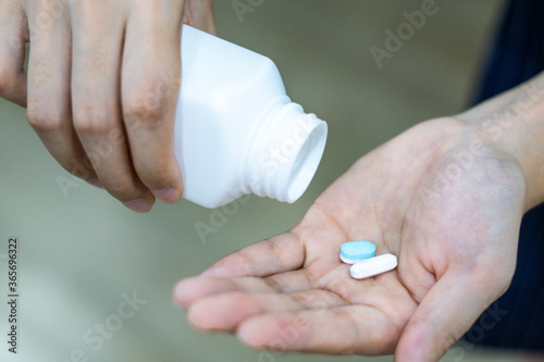 Female hand holding pills and white bottle.
