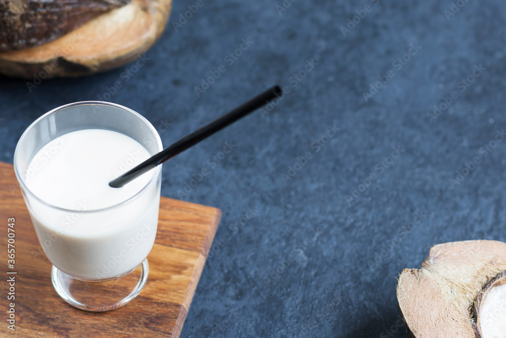 Coconut milk in a glass glass on a wooden board and coconuts on a dark background. Natural food product. Selective focus.
