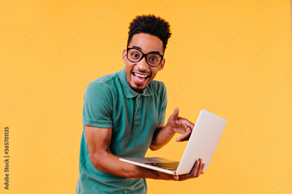 Blithesome student in green t-shirt posing with laptop. Indoor photo of amazed male freelancer isolated on yellow background. Blithesome student in green t-shirt posing with laptop. Indoor photo of amazed male freelancer isolated on yellow background.