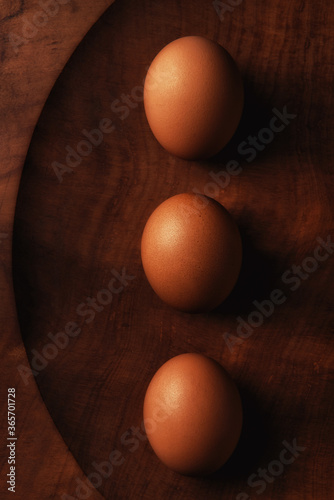 Three brown eggs inked up on a wood platter still life with warm side light.