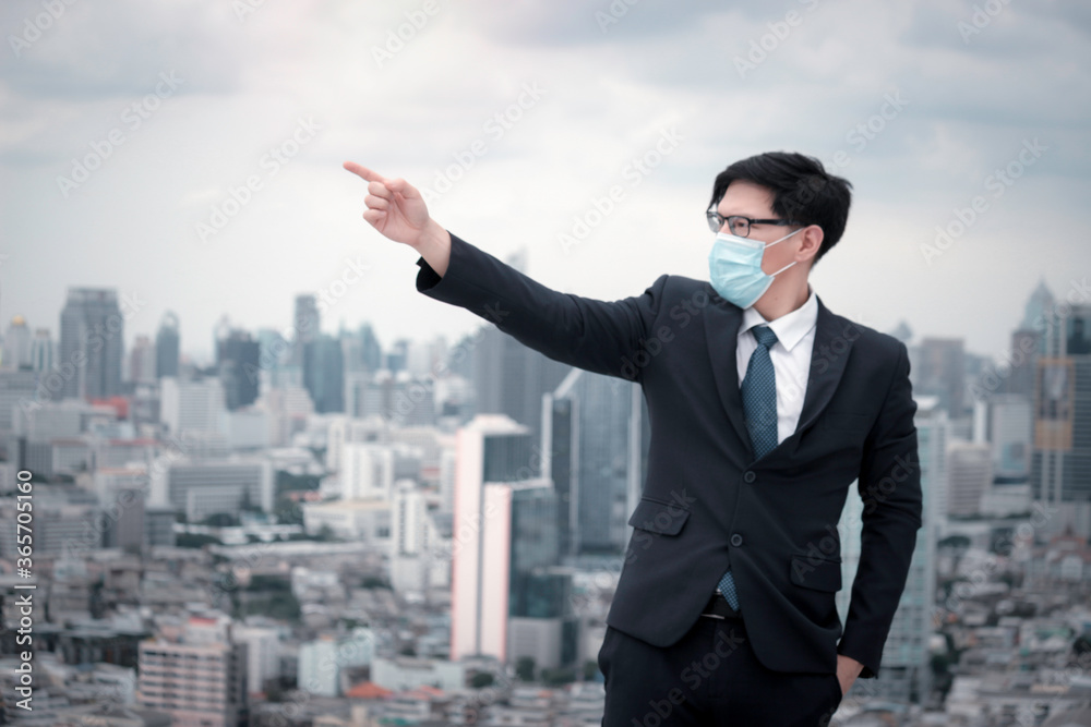 Young Asian businessman in suit wearing face mask to protect himself against virus or anti air dust pollution problem in city, man pointing to the sky with skyscraper city Young Asian businessman in suit wearing face mask to protect himself against virus or anti air dust pollution problem in city, man pointing to the sky with skyscraper city