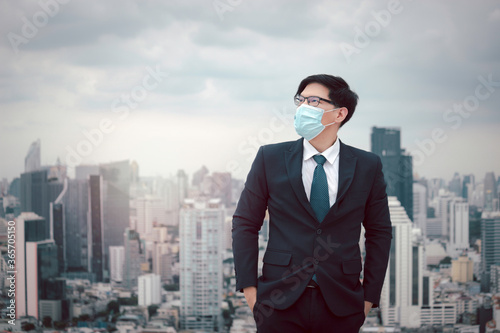 Young Asian businessman in suit wearing face mask to protect himself against virus with skyscraper city outdoor, or anti air dust pollution problem in city