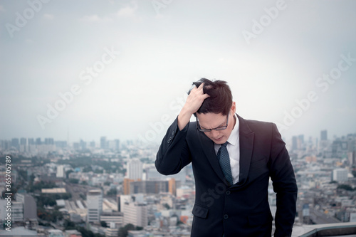 Young Asian businessman in suit with skyscraper city outdoor, stressed frustrated man putting his head in his hand thinking about his job, feeling disappointed or tired.