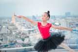Asian ballerina dancer girl practicing ballet dancing with colored smoke bomb on rooftop with skyscraper city view, adorable child dancing in ballet