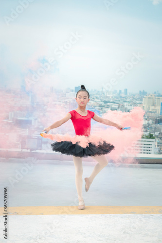 Asian ballerina dancer girl practicing ballet dancing with colored smoke bomb on rooftop with skyscraper city view, adorable child dancing in ballet © Stella