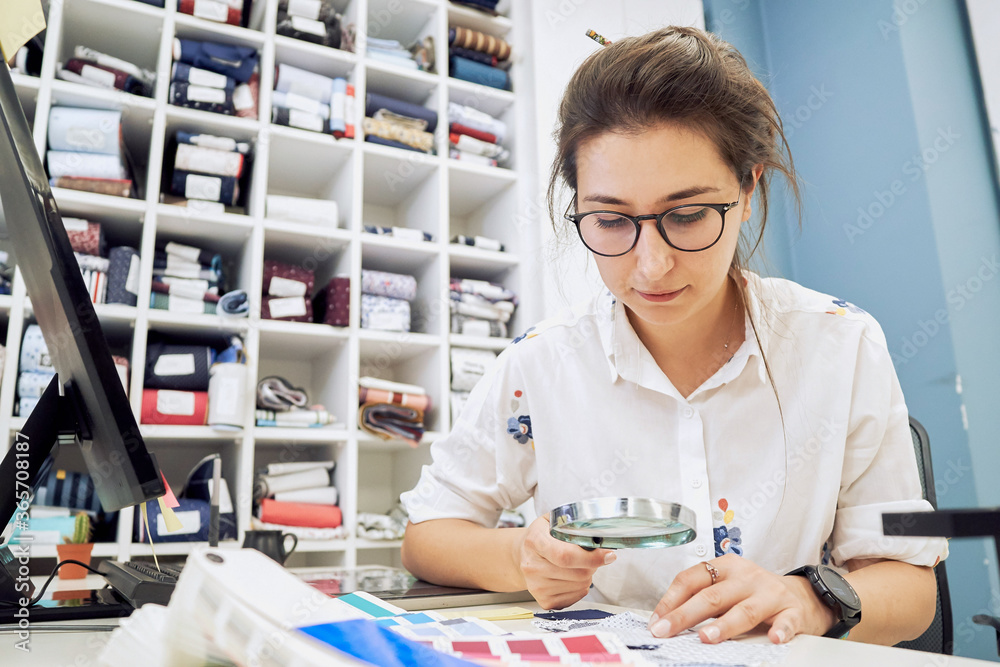 Female fashion designer holding color samples choosing fabric textile at workplace, dressmaker or tailor working at desk pointing at set palette making choice selection Female fashion designer holding color samples choosing fabric textile at workplace, dressmaker or tailor working at desk pointing at set palette making choice selection