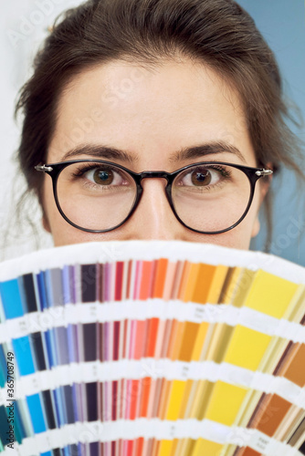 Young woman portrait, wearing glasses with color palette, close up portrait, only eyes are visible. Female model holding pantone chart.