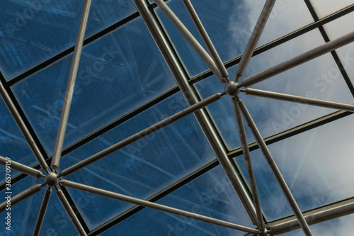 Elaborate steel metal greenhouse structure with diffuse view of deep blue sky with clouds  horizontal aspect