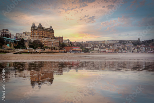 Victorian architecture of the Scarborough hotel reflected on the beach as the tide comes in at sunset