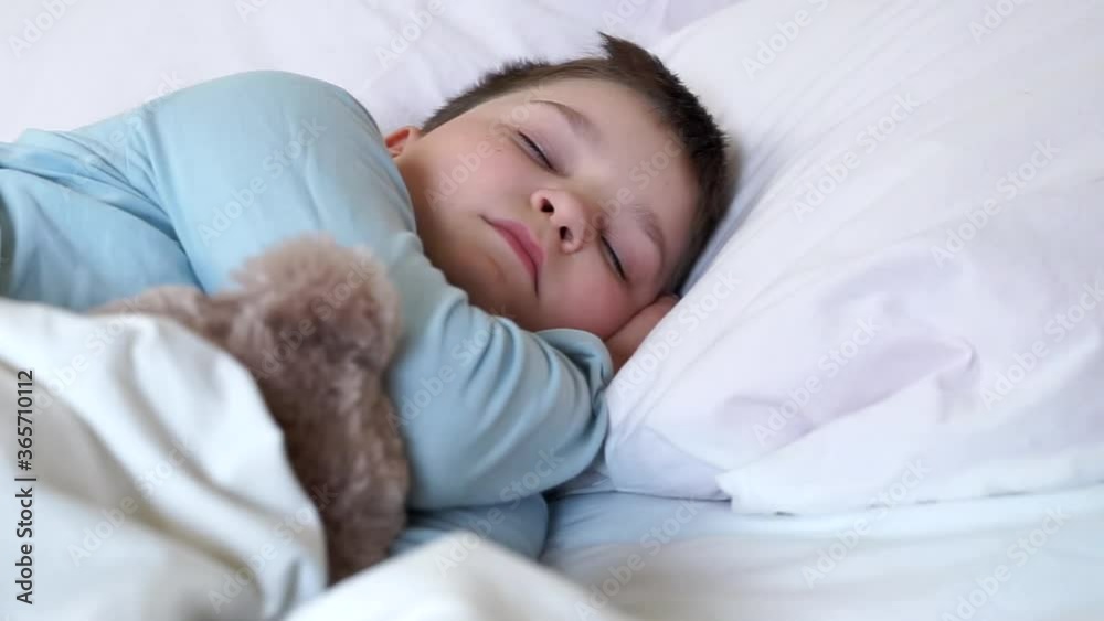 cute little child boy sleeping in cozy white bed lying on pillow with teddy bear toy. young baby kid sleeping covered with blanket on white sheets in bedroom. dreamy kid sleep in early morning cute little child boy sleeping in cozy white bed lying on pillow with teddy bear toy. young baby kid sleeping covered with blanket on white sheets in bedroom. dreamy kid sleep in early morning