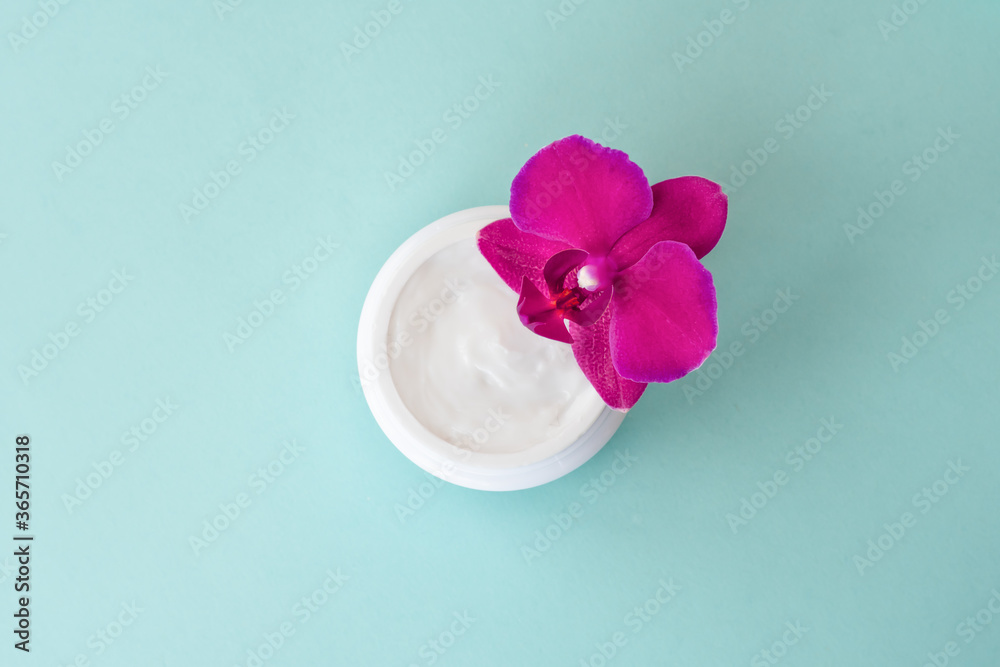 Cream in white jar on mint background with beautiful bright magenta orchid flowers. Soft cream with orchid extract for moisturizing skin. Eco cosmetic product, top view