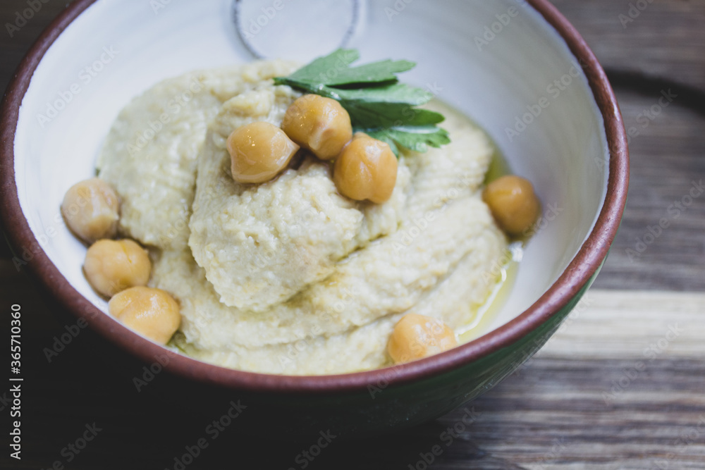 Hummus decorated with parsley and chickpea peas in a ceramic bowl on a wooden background 